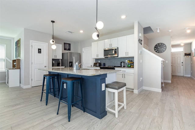 kitchen with pendant lighting, appliances with stainless steel finishes, white cabinetry, an island with sink, and a kitchen bar