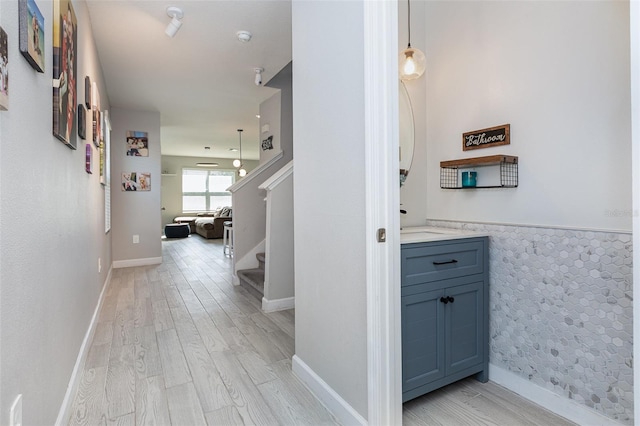 corridor featuring baseboards, stairway, a wainscoted wall, and light wood-style floors