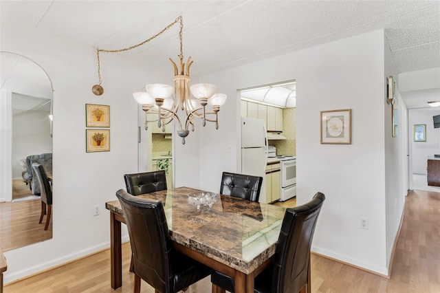 dining space with baseboards, light wood finished floors, arched walkways, and a notable chandelier