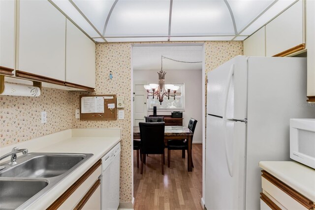 kitchen with a chandelier, white appliances, a sink, and white cabinets