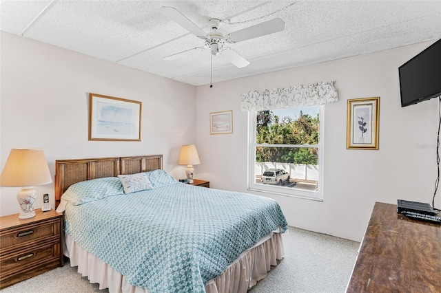 bedroom featuring a ceiling fan, light carpet, and a textured ceiling