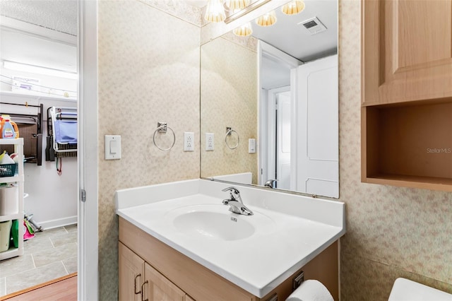 bathroom with wallpapered walls, visible vents, and vanity