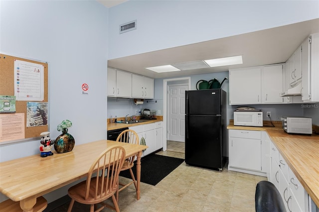 kitchen featuring visible vents, white microwave, freestanding refrigerator, white cabinetry, and under cabinet range hood
