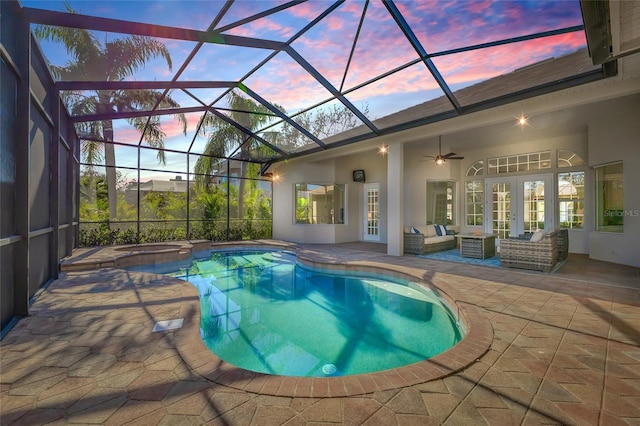 pool at dusk with a patio, glass enclosure, an outdoor living space, a ceiling fan, and french doors