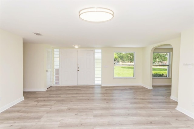 foyer featuring arched walkways, light wood-type flooring, visible vents, and baseboards