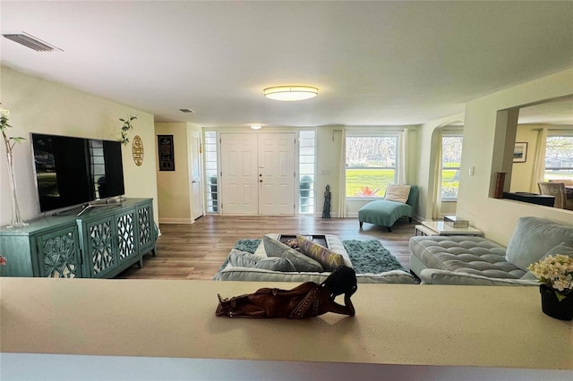 living area with a healthy amount of sunlight, visible vents, arched walkways, and wood finished floors