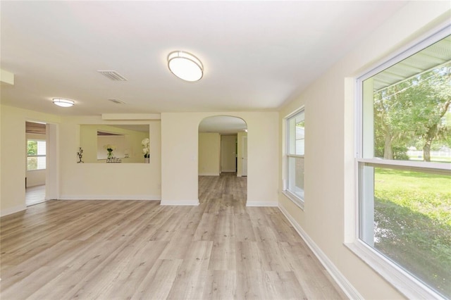 spare room featuring light wood-type flooring, visible vents, arched walkways, and baseboards