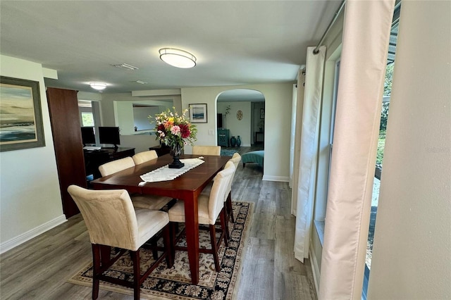 dining space with arched walkways, visible vents, baseboards, and wood finished floors