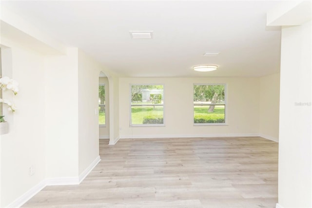 unfurnished room featuring arched walkways, baseboards, visible vents, and light wood finished floors