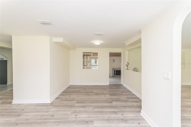 spare room with light wood-style floors, visible vents, arched walkways, and baseboards