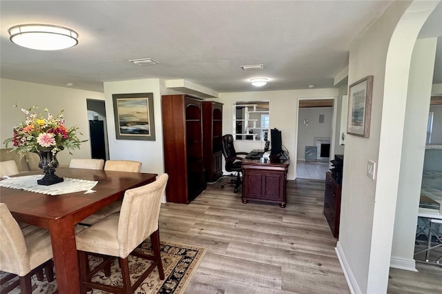 dining room with arched walkways, light wood-type flooring, visible vents, and baseboards