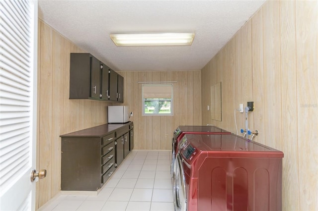 laundry room featuring cabinet space, wooden walls, washing machine and clothes dryer, a textured ceiling, and light tile patterned flooring