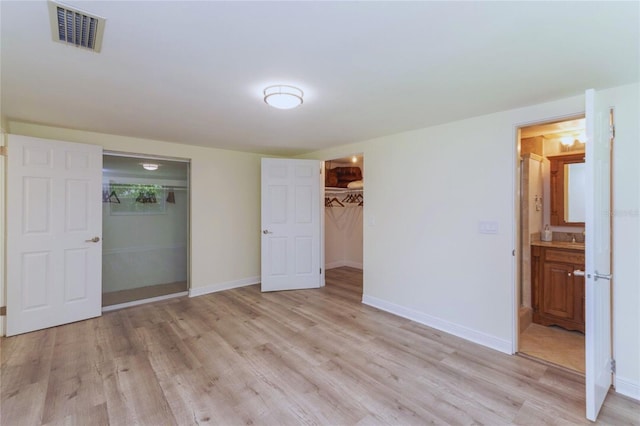 unfurnished bedroom with light wood-style floors, visible vents, ensuite bath, and baseboards