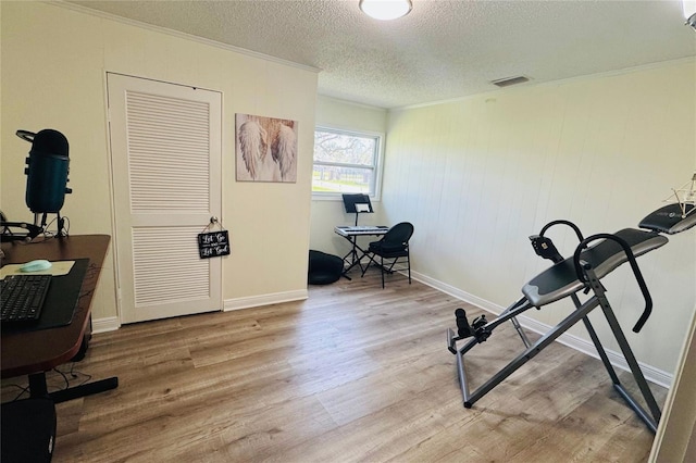 exercise room featuring ornamental molding, visible vents, a textured ceiling, and wood finished floors