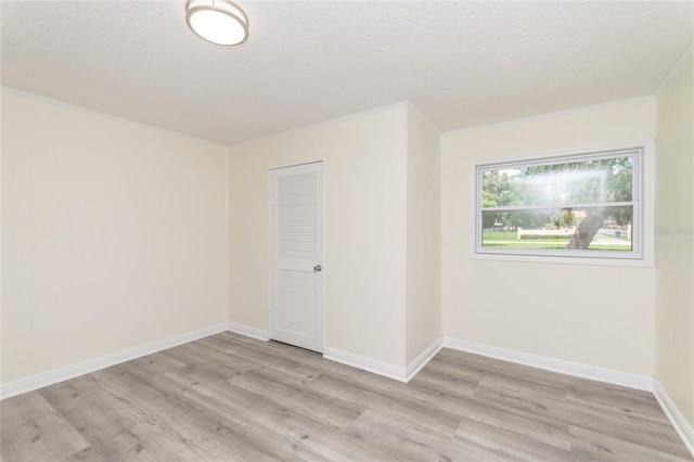 spare room featuring ornamental molding, baseboards, light wood-style flooring, and a textured ceiling