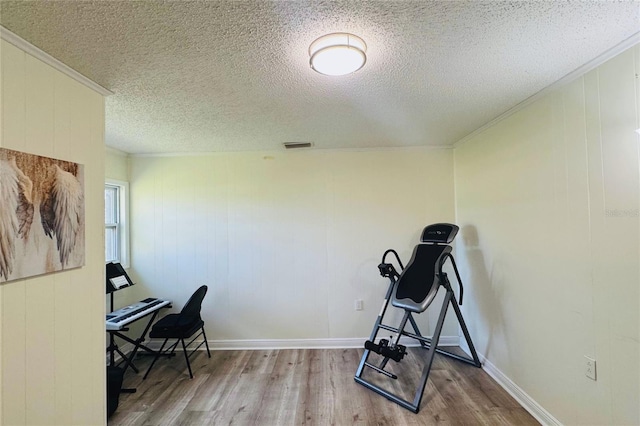 home office featuring light wood-style flooring, visible vents, ornamental molding, and a textured ceiling