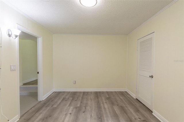 empty room featuring a textured ceiling, ornamental molding, light wood-style flooring, and baseboards