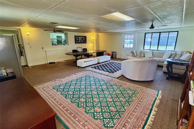 carpeted living area with a ceiling fan and a drop ceiling