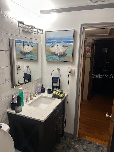 half bathroom with tile walls, tasteful backsplash, visible vents, toilet, and vanity