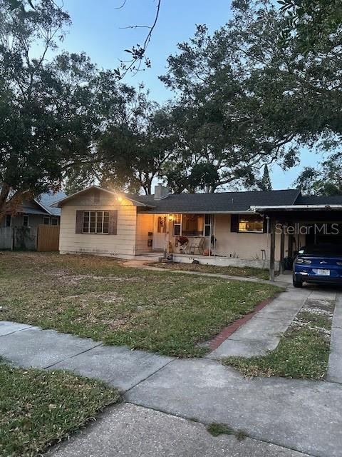 ranch-style home with fence, concrete driveway, a carport, a front lawn, and a chimney