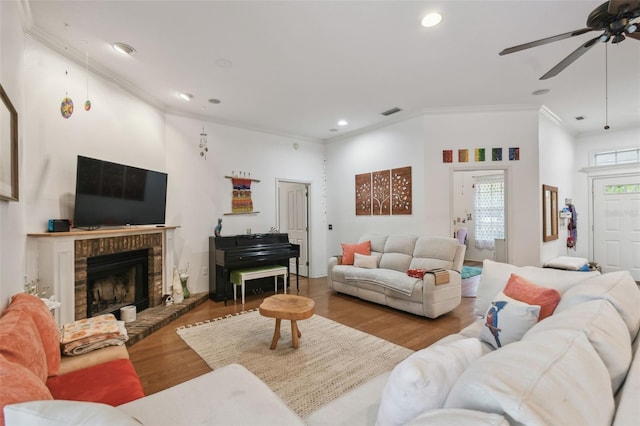 living room featuring recessed lighting, wood finished floors, a ceiling fan, a brick fireplace, and crown molding