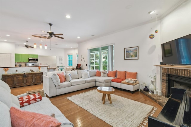 living area with light wood finished floors, a brick fireplace, and recessed lighting