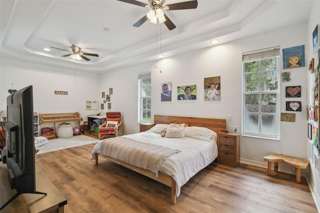 bedroom with light wood-type flooring, a raised ceiling, and multiple windows