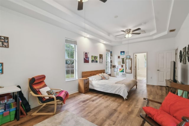 bedroom with a tray ceiling, visible vents, ensuite bathroom, wood finished floors, and baseboards