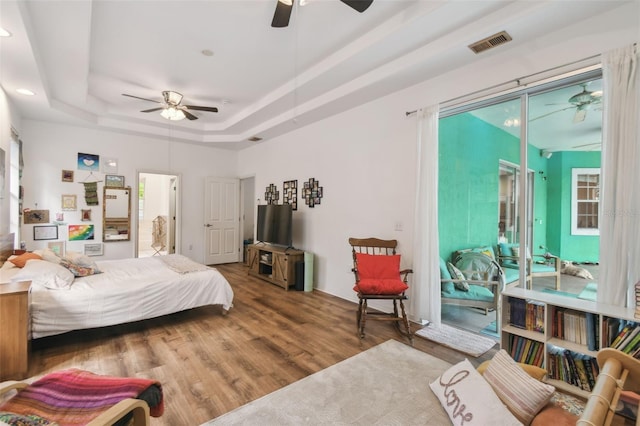 bedroom with visible vents, a raised ceiling, a ceiling fan, wood finished floors, and access to exterior