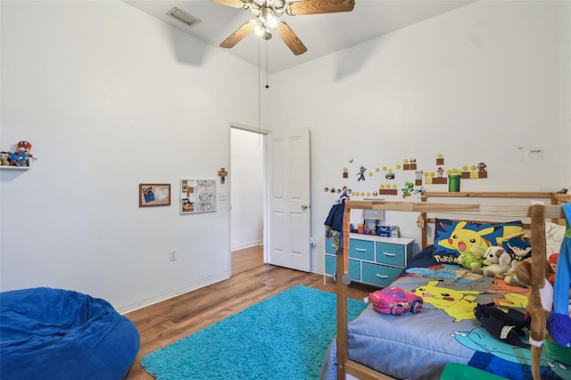 bedroom featuring a high ceiling, wood finished floors, a ceiling fan, visible vents, and baseboards