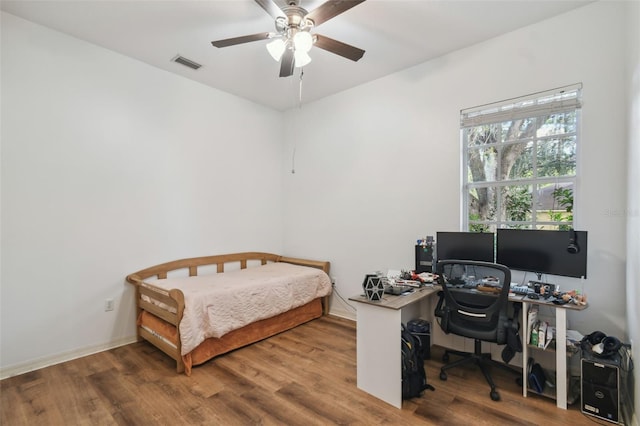 bedroom with a ceiling fan, visible vents, baseboards, and wood finished floors