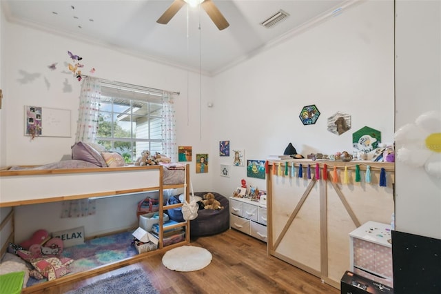 bedroom with a ceiling fan, visible vents, crown molding, and wood finished floors