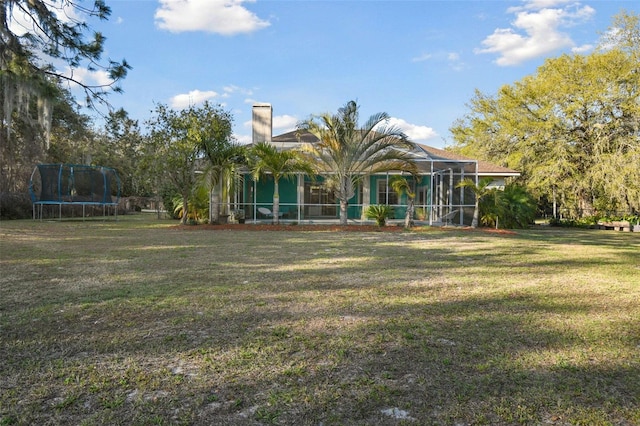 back of house featuring a trampoline, a chimney, a lanai, and a lawn