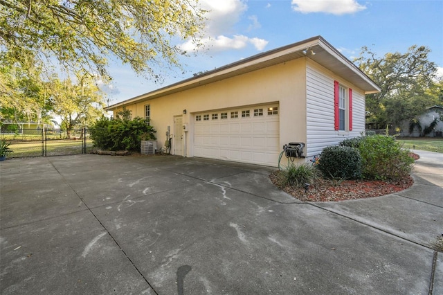 view of side of home with an attached garage, central AC, fence, concrete driveway, and stucco siding