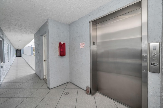 hall with elevator, a textured ceiling, and light tile patterned floors