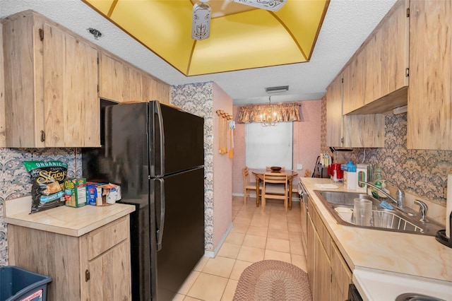 kitchen featuring sink, light tile patterned floors, black refrigerator, hanging light fixtures, and light brown cabinetry