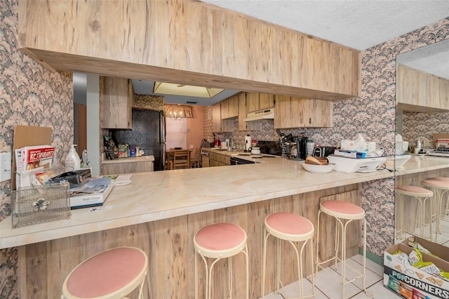 kitchen with a breakfast bar area, electric range, a textured ceiling, decorative backsplash, and kitchen peninsula