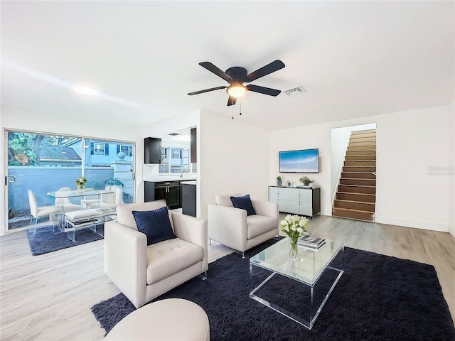 living area with visible vents, stairway, light wood-style floors, a ceiling fan, and baseboards