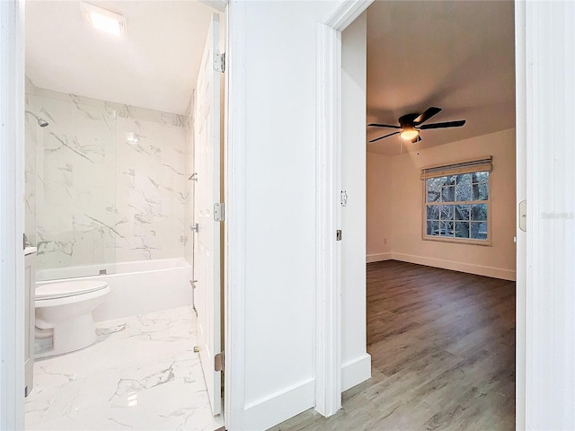 full bath with baseboards, a ceiling fan, toilet, marble finish floor, and tub / shower combination