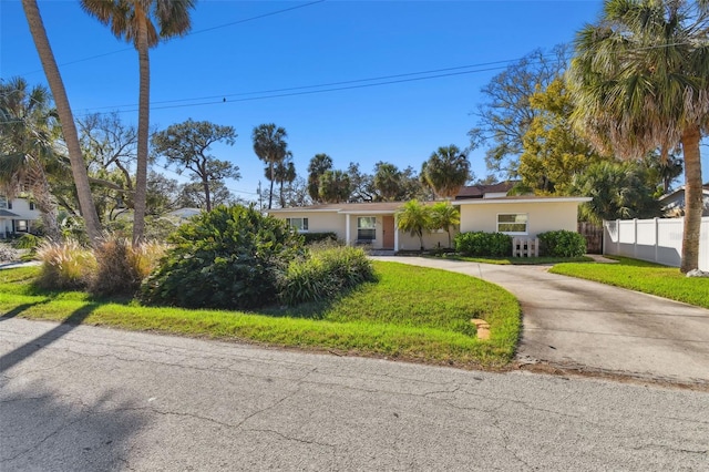 view of front facade featuring concrete driveway, a front lawn, fence, and stucco siding