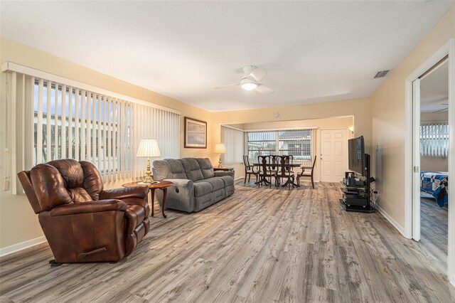 living area featuring visible vents, ceiling fan, baseboards, and wood finished floors