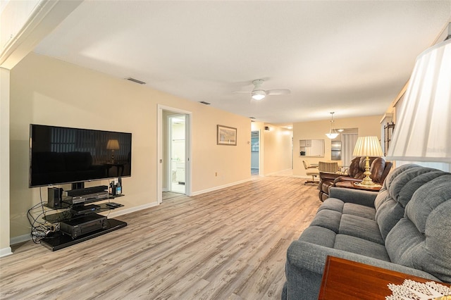 living room featuring light wood finished floors, baseboards, visible vents, and a ceiling fan