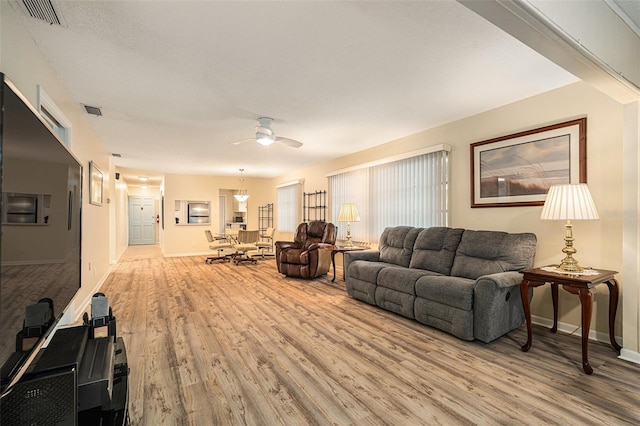 living area featuring baseboards, a ceiling fan, visible vents, and light wood-style floors