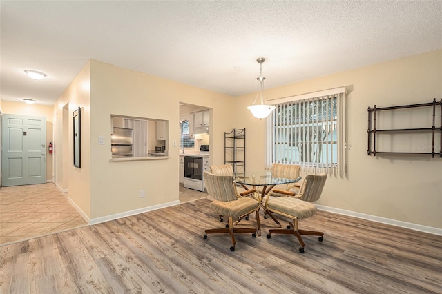 dining room featuring light wood finished floors, baseboards, and a textured ceiling