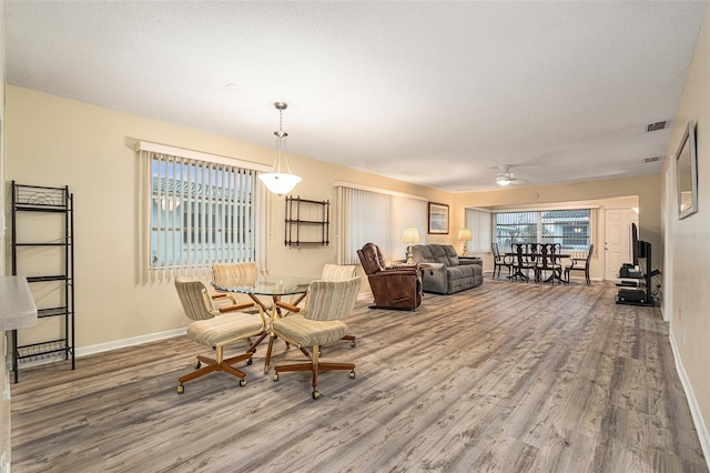 interior space with a textured ceiling, ceiling fan, wood finished floors, visible vents, and baseboards