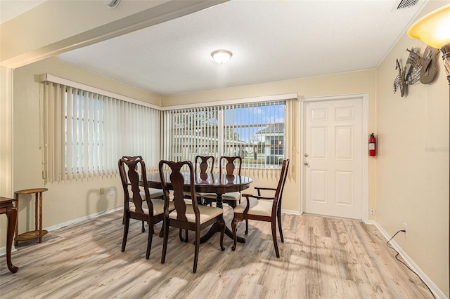 dining room with light wood-style floors, visible vents, a textured ceiling, and baseboards