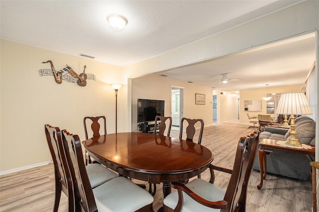 dining space featuring light wood finished floors, baseboards, visible vents, ceiling fan, and a textured ceiling