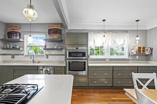 kitchen with appliances with stainless steel finishes, sink, light wood-type flooring, pendant lighting, and ornamental molding