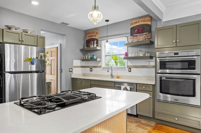 kitchen with sink, stainless steel appliances, green cabinetry, hanging light fixtures, and tasteful backsplash