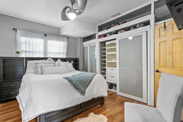 bedroom featuring hardwood / wood-style flooring, ceiling fan, and two closets